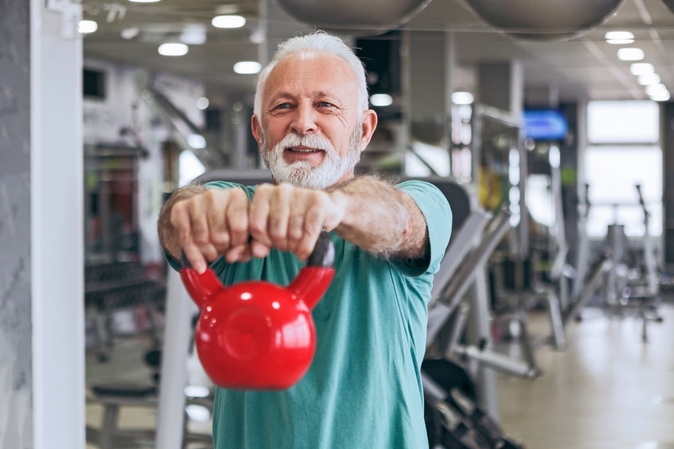 older man lifting a kettlebell strength training for seniors at gym near me in monroe